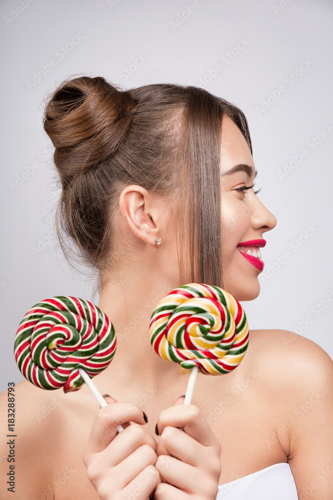 Naklejka premium Beauty fashion model with colourful lollipops. Young pretty woman with pink lips and makeup. Candies like a sunglasses