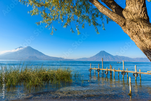 Fototapeta Naklejka Na Ścianę i Meble -  Wooden pier at Lake Atitlan on the shore at Panajachel, Guatemala.  With beautiful landscape scenery of volcanoes Toliman, Atitlan and San Pedro in the background.