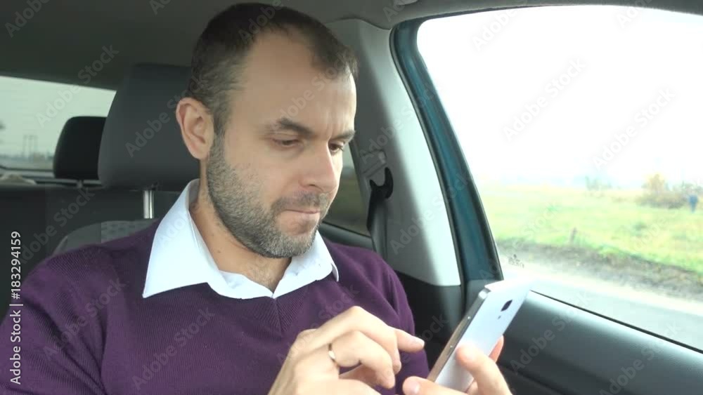Businessman using a smartphone while sitting inside car. Man with a smart-phone in the vehicle. Businessman using a smartphone while sitting inside car. Man with a smart-phone in the vehicle.