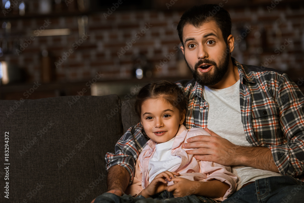 surprised father and daughter sitting on couch and watching tv at home surprised father and daughter sitting on couch and watching tv at home
