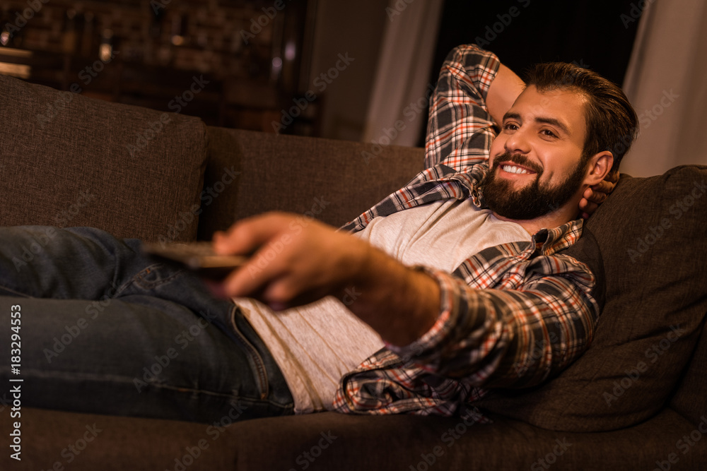 young man laying on couch and watching tv at home