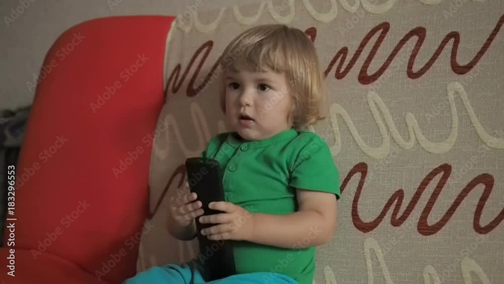 Little girl watching TV sitting on sofa with remote control in hand. Cute child with sitting on living room sofa and watching tv. Little girl watching TV sitting on sofa with remote control in hand. Cute child with sitting on living room sofa and watching tv.