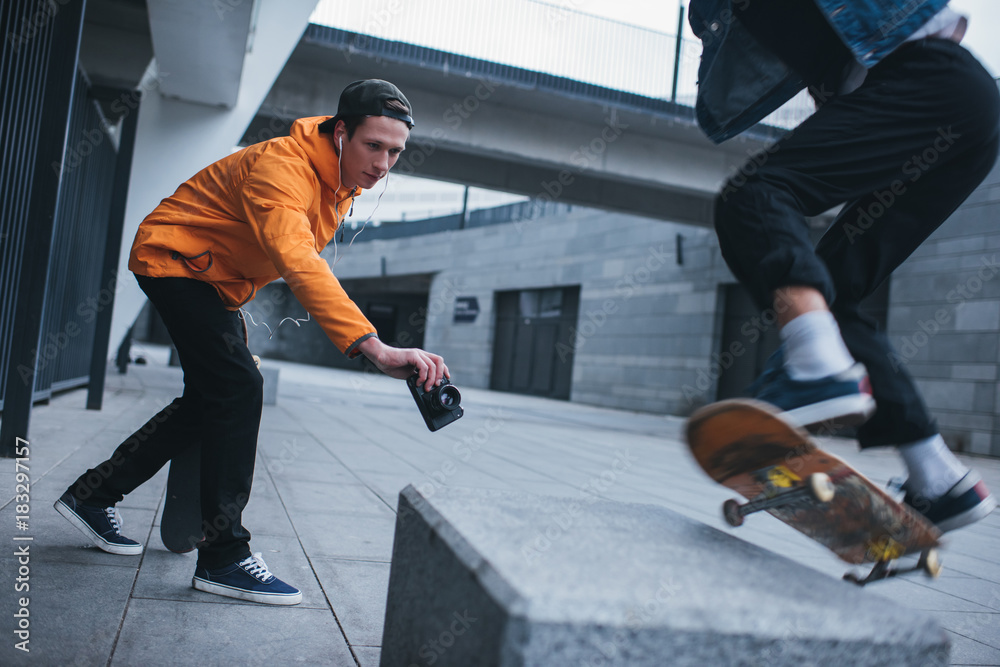 Obraz premium skateboarder taking photo of his partner doing trick outdoors