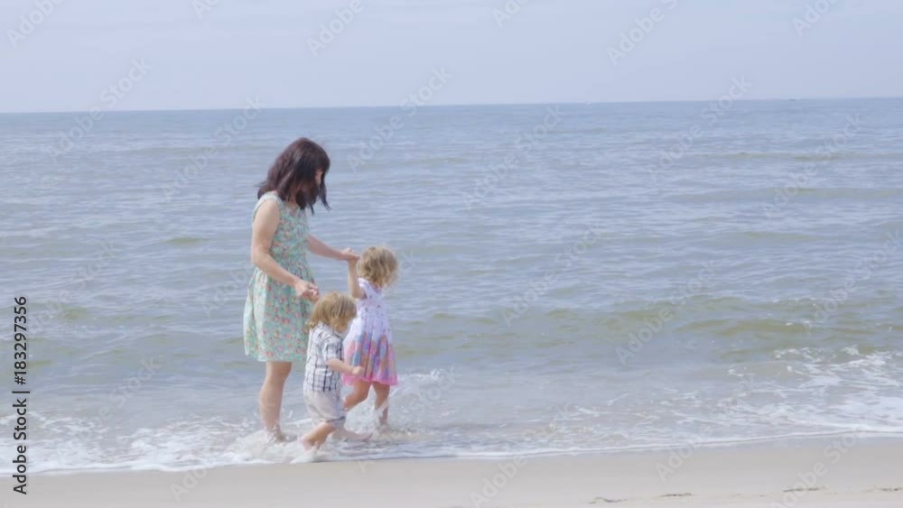 Happy family on the beach. Mother holds the arms of her son and daughter walking along the seashore. Slow motion. Happy family on the beach. Mother holds the arms of her son and daughter walking along the seashore. Slow motion.