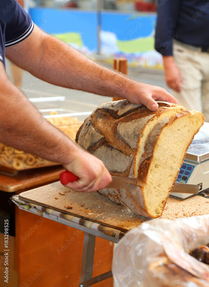 baker cuts a large loaf of baked bread into the bakery baker cuts a large loaf of baked bread into the bakery