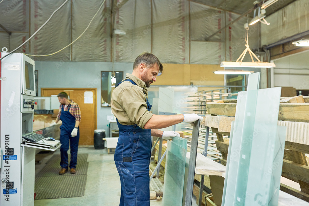 Side view portrait of mature man working in industrial workshop choosing material for cutting, wood and glass, copy space Side view portrait of mature man working in industrial workshop choosing material for cutting, wood and glass, copy space