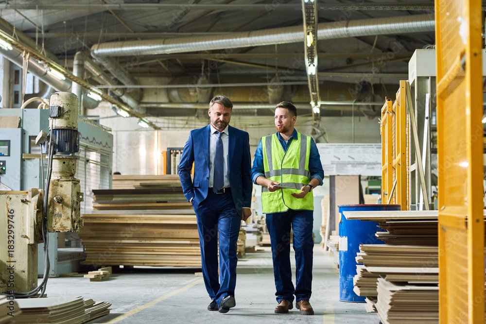 Full length portrait of young workman giving tour of modern factory to handsome mature businessman discussing possible investment, copy space - obrazy, fototapety, plakaty 