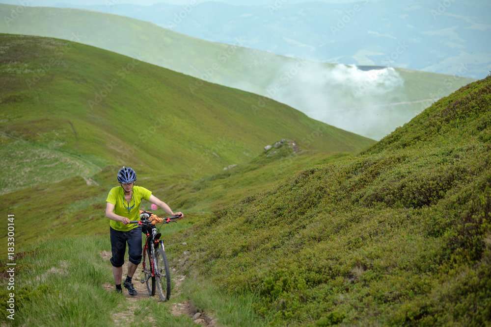 Biker pushes bicycle up in the mountains