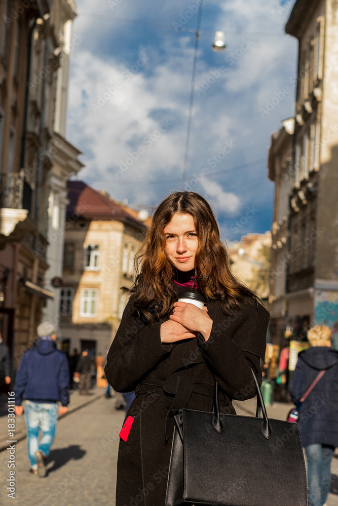 Bright girl posing with coffee in the hands of the street