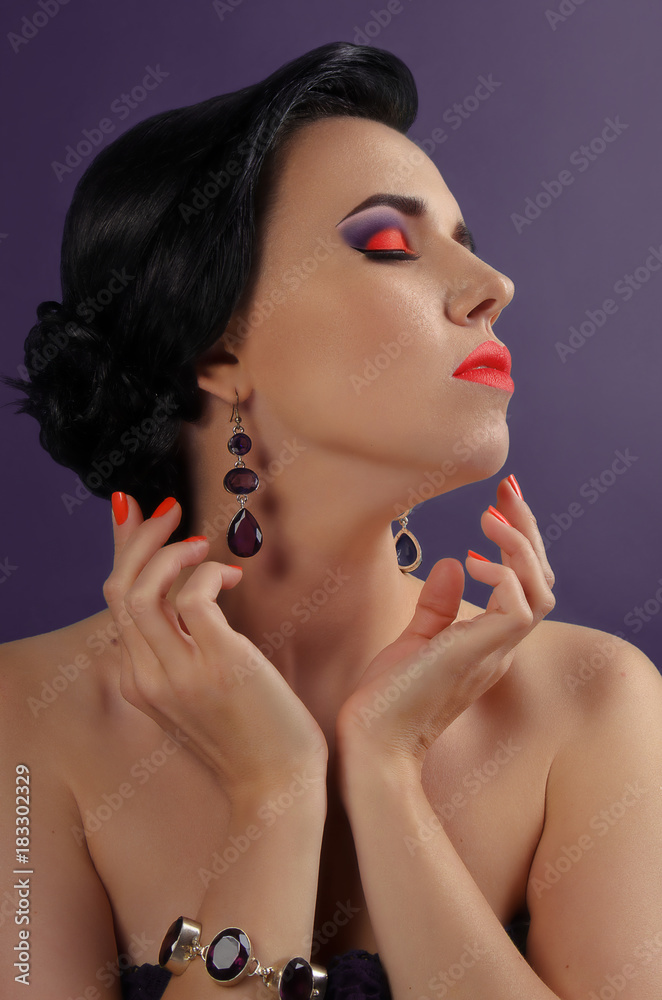 Bright colorful makeup in vivid colors on young attractive womens face. Beauty, portrait with orange and violet eyeshadows and oramge lips. Sensual posing with hands. Cosmetics, healthy skin.