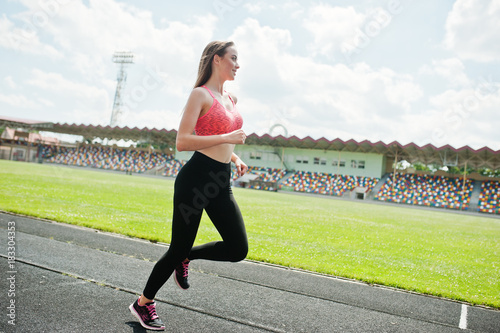 Fitness sporty girl in sportswear at stadium outdoor sports. Happy sexy woman running on athletic track treadmill on stadium.