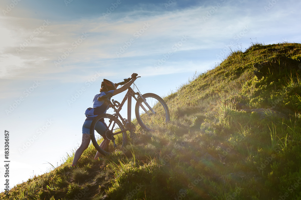 Fototapeta premium Biker pushes bicycle up in the mountains
