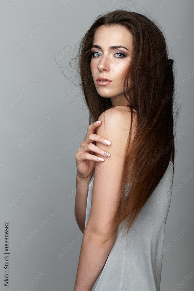 Naklejka premium Beauty portrait of young woman. Brunette girl with long disheveled flying hair and day female makeup on gray background