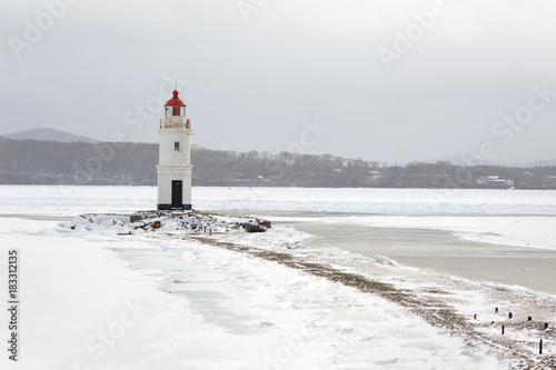 Red and white lighthouse at winter snowy sea coast.