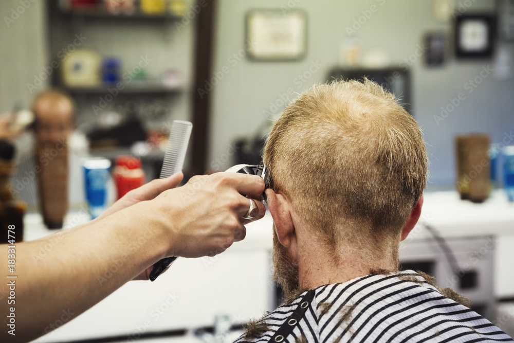 A customer sitting in the barber's chair, and a barber using an electric shaver to shave his head. A customer sitting in the barber's chair, and a barber using an electric shaver to shave his head.