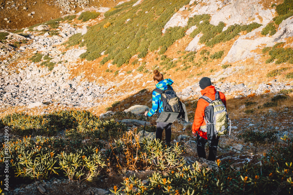 Couple of hikers in the mountains. Tourists woman and man descend from the mountain Couple of hikers in the mountains. Tourists woman and man descend from the mountain