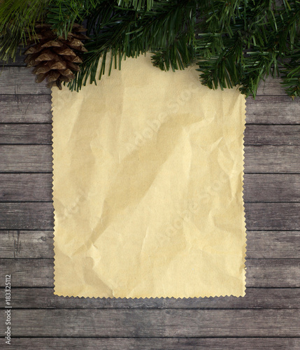 Christmas composition with fir tree, cones and sheet of writing paper. Wooden plank background.