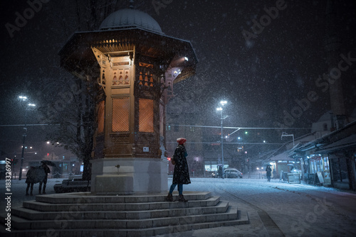 Sebilj in Sarajevo on snowy night and girl walking down the steps  photo