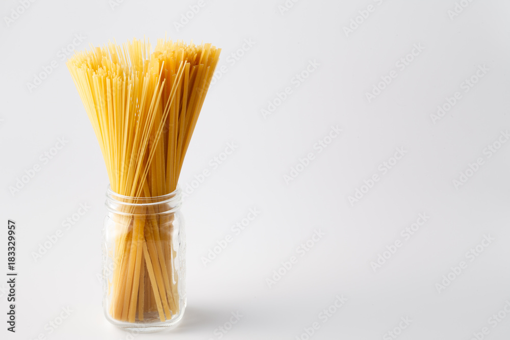 Heap of uncooked italian pasta in glass jar on white with copy space
