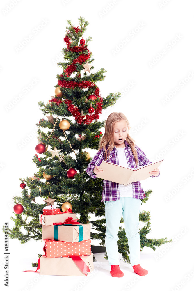 Portrait of cute little girl reading book near Christmas tree on white background Portrait of cute little girl reading book near Christmas tree on white background