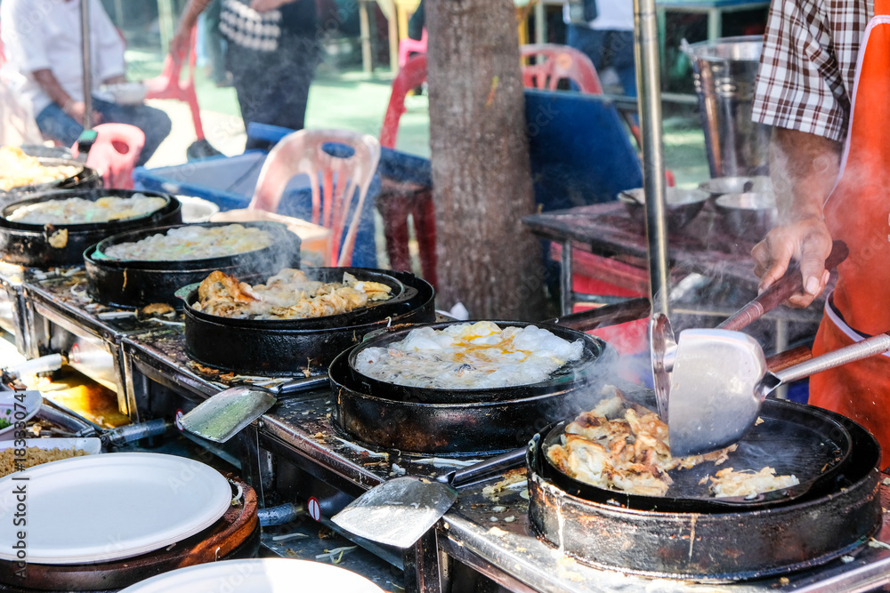 He is cooking fried mussel pancakes with egg on the first pan with some smoke and waiting for other pans He is cooking fried mussel pancakes with egg on the first pan with some smoke and waiting for other pans