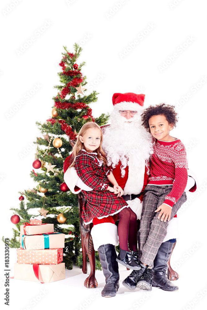 Santa Claus sitting in chair near Christmas tree with multi-ethnic boy and girl on his lap Santa Claus sitting in chair near Christmas tree with multi-ethnic boy and girl on his lap