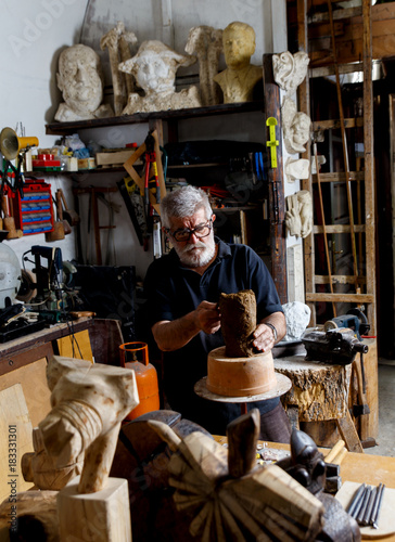 Senior sculptor working on his clay sculpture in his workshop.