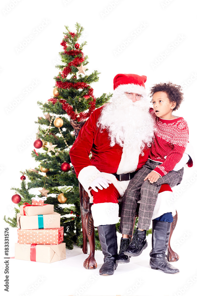 Mixed race little boy talking with Santa Claus sitting on his lap near Christmas tree Mixed race little boy talking with Santa Claus sitting on his lap near Christmas tree