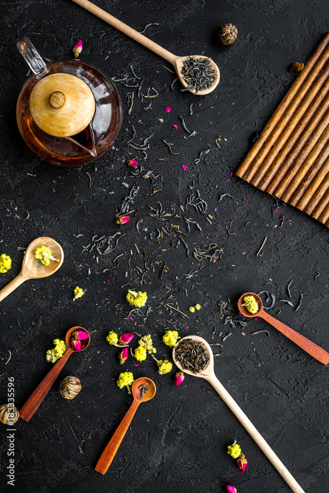 Brew the aromatic tea. Tea pot near wooden spoons with dried tea leaves, flowers and spices on black wooden background top view copyspace Brew the aromatic tea. Tea pot near wooden spoons with dried tea leaves, flowers and spices on black wooden background top view copyspace