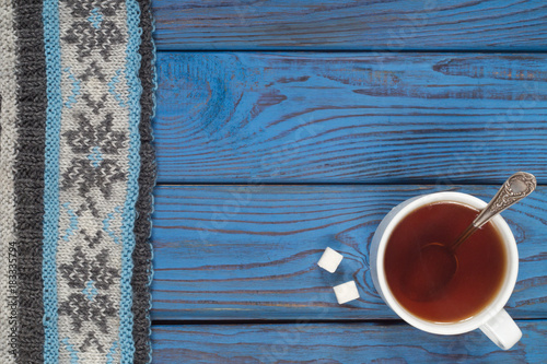 A cup of tea and a knitted scarf on the background of a blue woo