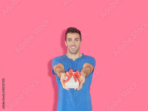 Handsome caucasian guy holding gift box standing in front of pink background. photo