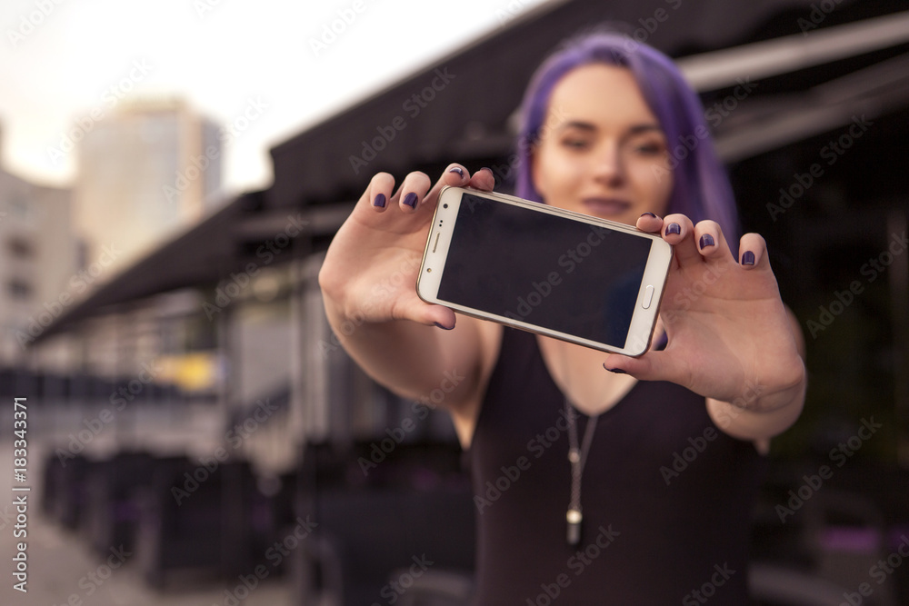 Beautiful brunette woman with colored (purple violet blue) hair in dark black slim dress outdoor in the european city, smiling making selfie on her phone