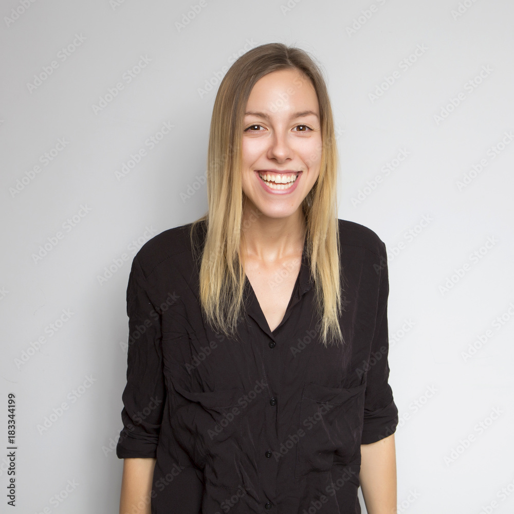 Beautiful brunette caucasian woman in dark black blouse with bright emotions standing on a neutral grey background. Her hands make a gesture. She smiling happily Beautiful brunette caucasian woman in dark black blouse with bright emotions standing on a neutral grey background. Her hands make a gesture. She smiling happily
