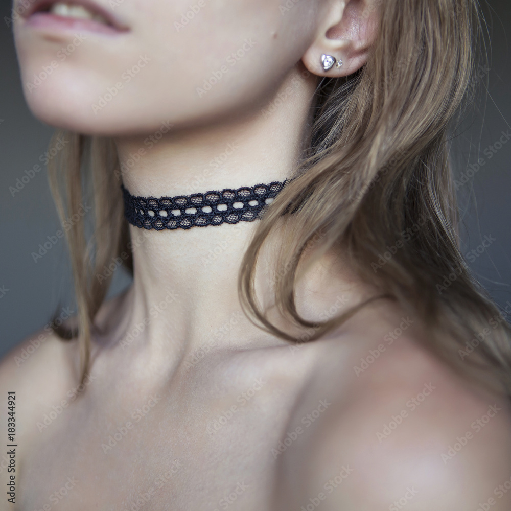 Beautiful woman with a long hair and sensual lips, showing her neck with a choker jewelry on it. Naked flawless skin (collarbones), soft day light, neutral gray background. Square picture