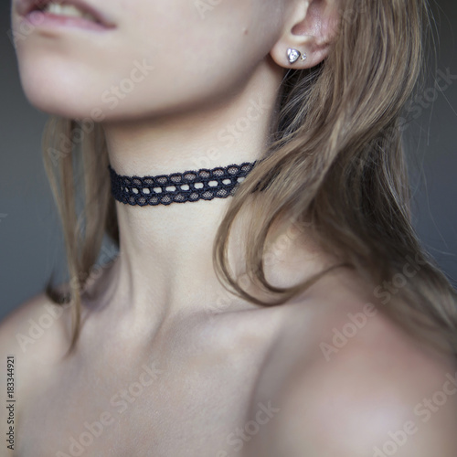 Beautiful woman with a long hair and sensual lips, showing her neck with a choker jewelry on it. Naked flawless skin (collarbones), soft day light, neutral gray background. Square picture