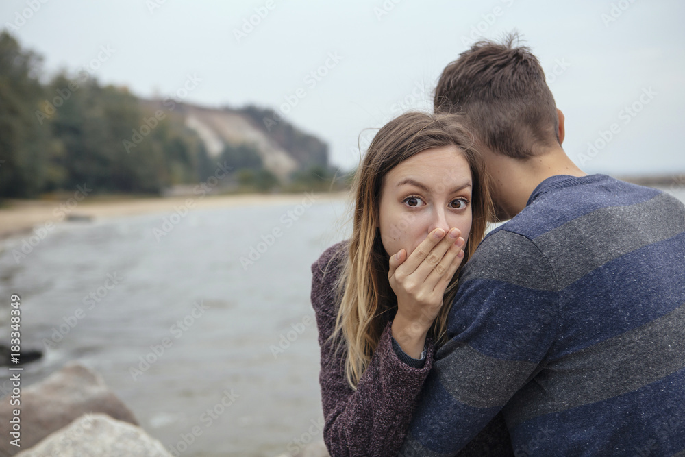 Happy thoughtful couple sitting on a rock beach near sea hugging each other in cold foggy cloudy autumn weather. Copy space Happy thoughtful couple sitting on a rock beach near sea hugging each other in cold foggy cloudy autumn weather. Copy space
