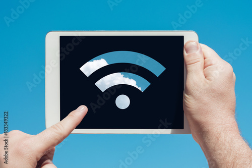 Man holding a tablet device showing wifi sign and touching the screen with a finger with blue sky in background
