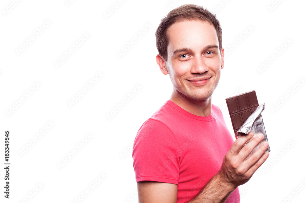 Sweet tooth concept. Portrait of smiling handsome young guy holding tablet of milk chocolate wrapped in silver foil and posing over white background. Copy-space. Close up. Studio shot