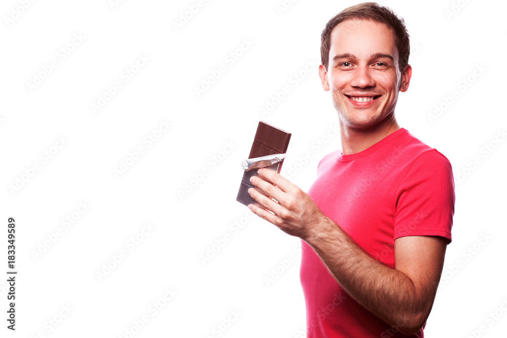 Sweet tooth concept. Portrait of smiling handsome young guy holding tablet of milk chocolate wrapped in silver foil and posing over white background. Copy-space. Close up. Studio shot Sweet tooth concept. Portrait of smiling handsome young guy holding tablet of milk chocolate wrapped in silver foil and posing over white background. Copy-space. Close up. Studio shot