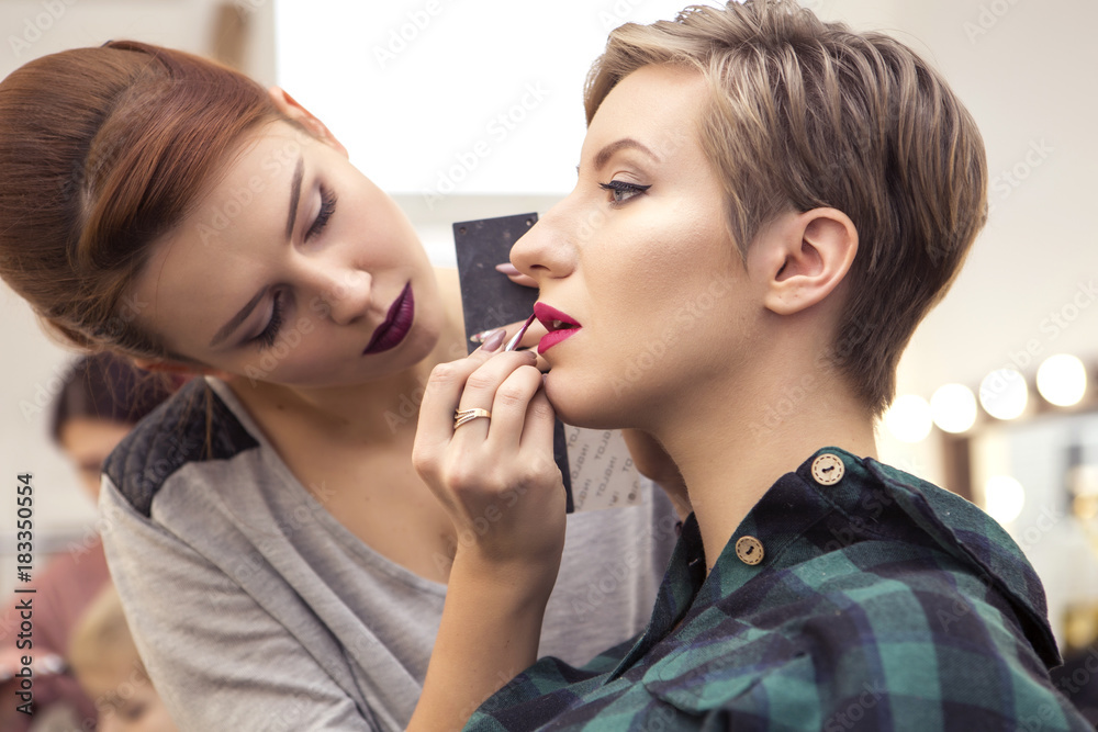 Gorgeous brunette woman makeup artist apply make up to a beautiful pregnant woman with short hairstyle for a photosession. Backstage. Copy space