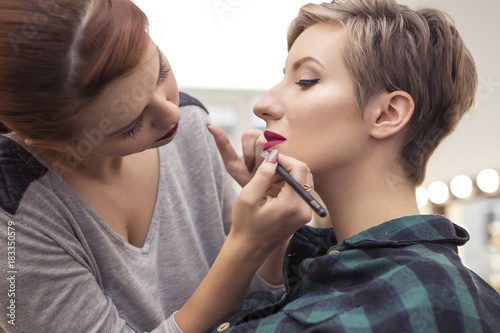 Gorgeous brunette woman makeup artist apply make up to a beautiful pregnant woman with short hairstyle for a photosession. Backstage. Copy space