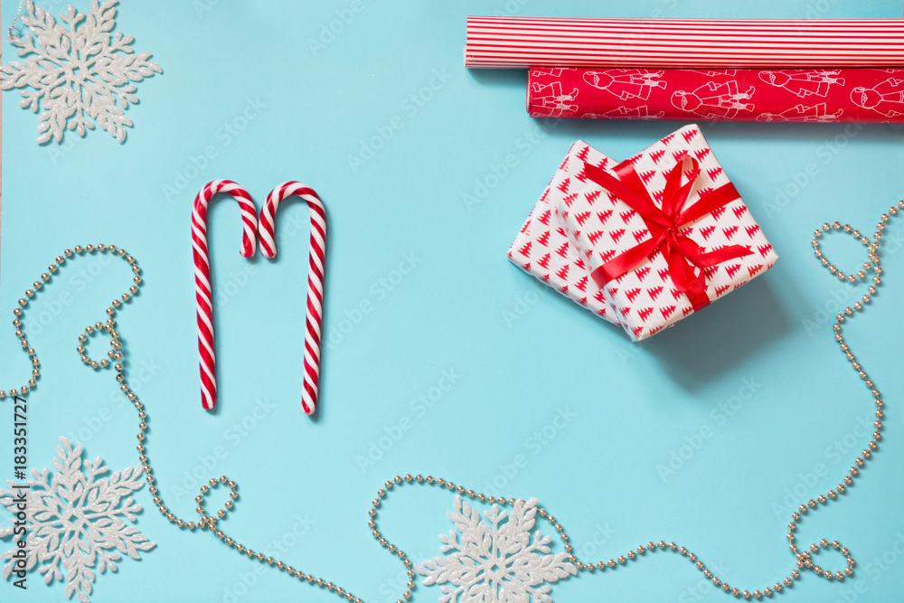 Obraz premium Christmas creative workplace with gift, snowflakes red wrapping paper on blue. Copy space. Holiday card.