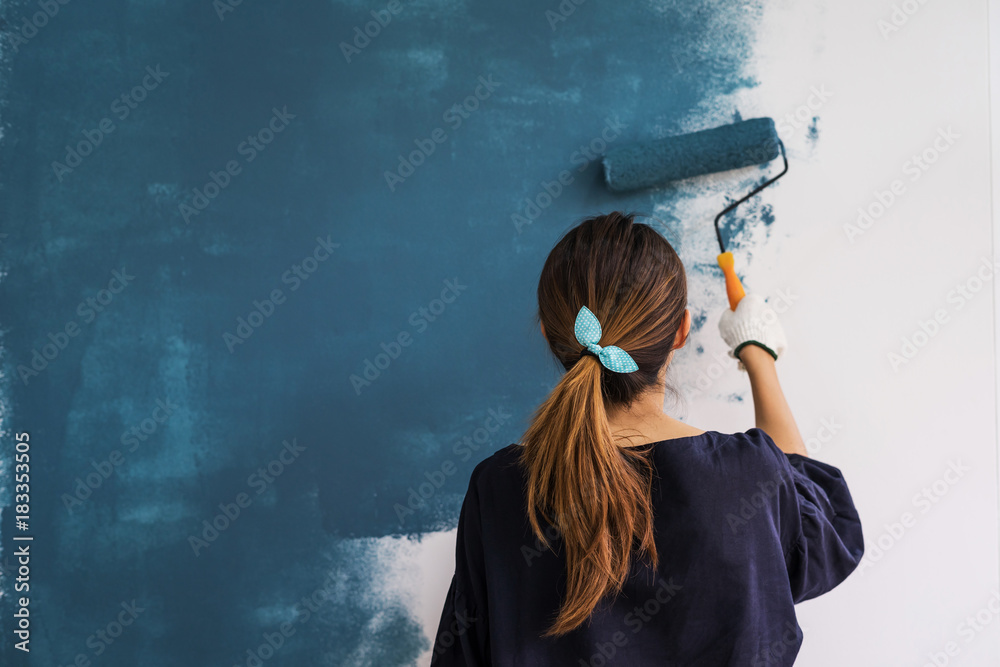 Young asian happy woman painting interior wall with paint roller in new house, Home decoration concept - obrazy, fototapety, plakaty 