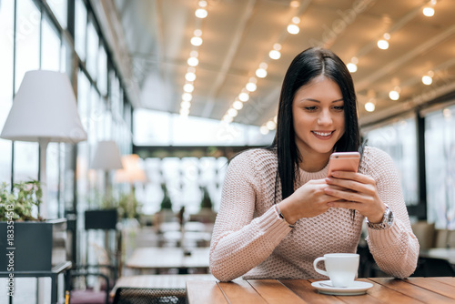 Obraz na plátne Young woman in a modern cafe reading a text message from her mobile phone