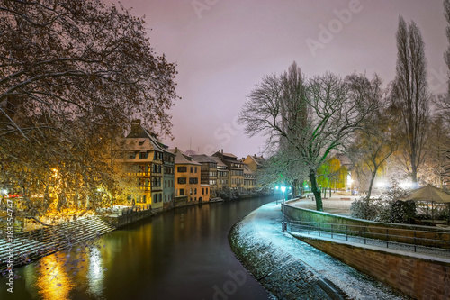 Old timber-framing houses in Petite France quarter, Strasbourg. Snow-covered roofs and refctions in the river water. Night scene.