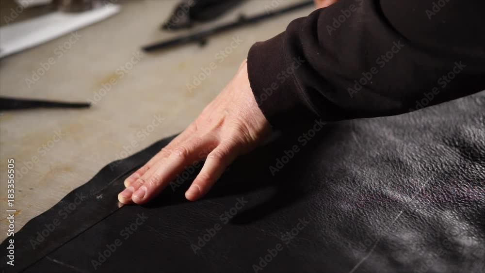 Skilled craftsman is using working tools to cut off a piece of leather. He is applying the ruler to the leather to cut smoothly. Skilled craftsman is using working tools to cut off a piece of leather. He is applying the ruler to the leather to cut smoothly.