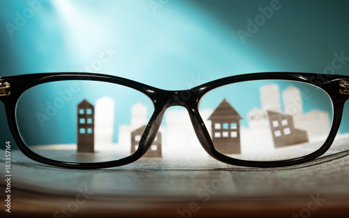 Eyeglasses lie on the open newspaper with paper houses. Concept of rent, search, purchase real estate.