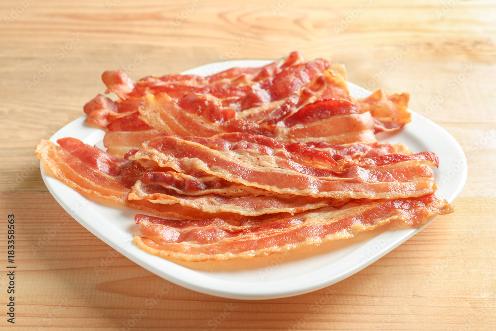 Plate with cooked bacon rashers on wooden table
