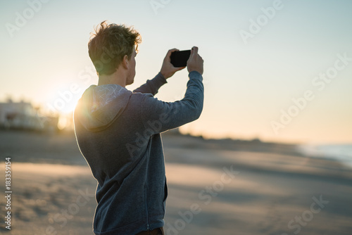 Man playing with phone at sunrise on a beach in Portugal