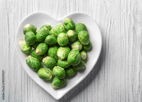 Heart-shaped plate with raw fresh Brussels sprouts on wooden background